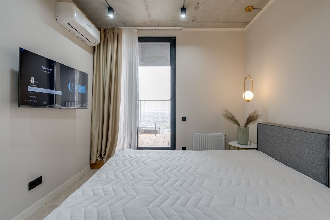 about-img Minimalistic bedroom featuring a balcony, flat screen TV, and elegant lighting.